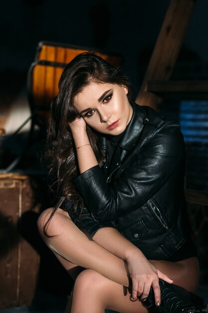 Portrait of a sexy girl with naked legs and in leather jacket posing in dark studio