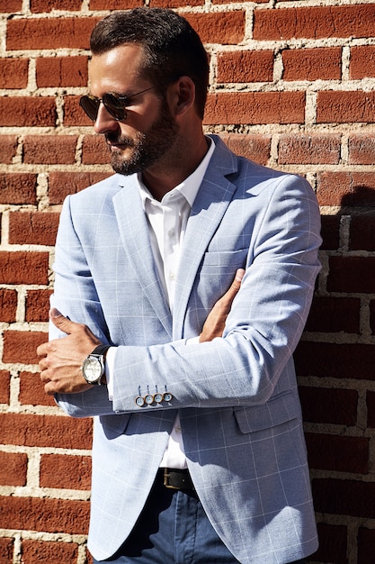 Free photo portrait of sexy handsome fashion businessman model dressed in elegant blue suit posing near brick wall on the street background. metrosexual