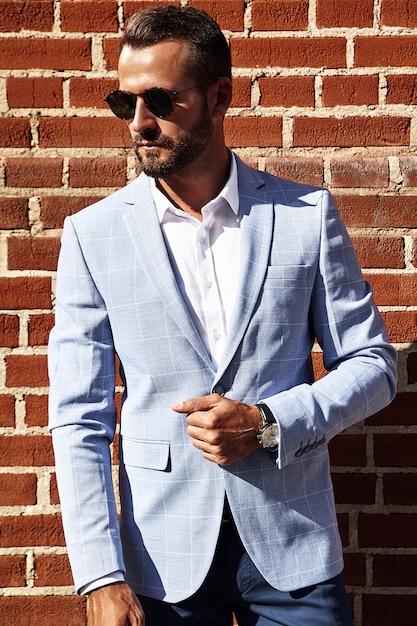 Free photo portrait of sexy handsome fashion businessman model dressed in elegant blue suit posing near brick wall on the street background. metrosexual