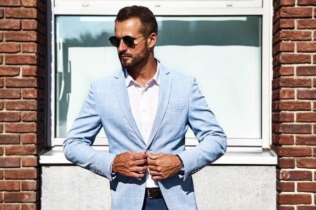 Free photo portrait of sexy handsome fashion businessman model dressed in elegant blue suit posing on street background. metrosexual