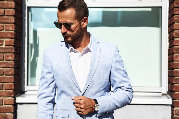 Free photo portrait of sexy handsome fashion businessman model dressed in elegant blue suit posing on street background. metrosexual