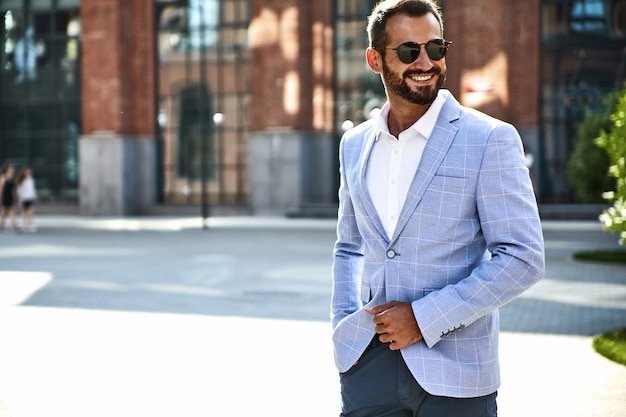 Portrait of sexy handsome fashion businessman model dressed in elegant blue suit posing on street background. Metrosexual