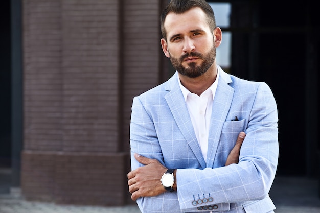 Free photo portrait of sexy handsome fashion businessman model dressed in elegant blue suit posing on street background. metrosexual