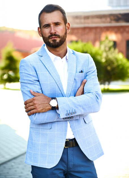 Portrait of sexy handsome fashion businessman model dressed in elegant blue suit posing on street background. Metrosexual