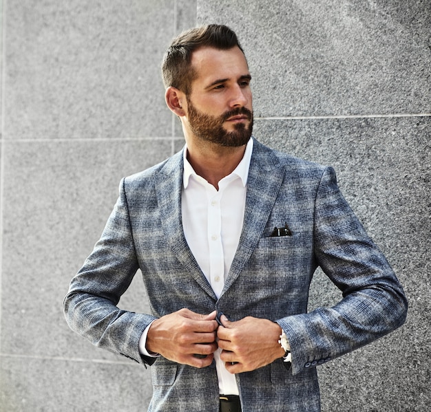 Portrait of sexy handsome fashion businessman model dressed in elegant checkered suit posing near gray wall on street background. Metrosexual