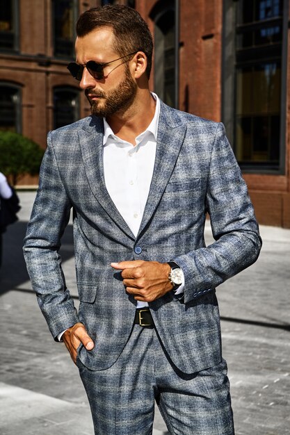 Portrait of sexy handsome fashion businessman model dressed in elegant checkered suit posing on street background. Metrosexual