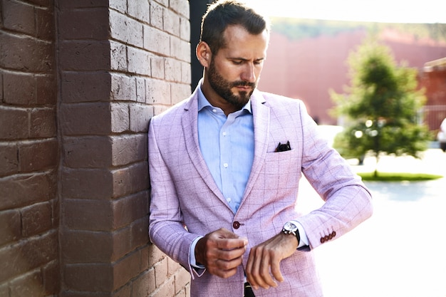 Free photo portrait of sexy handsome fashion businessman model dressed in elegant suit posing near brick wall on the street background. metrosexual