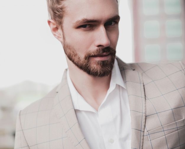 portrait of sexy handsome fashion male model man dressed in elegant beige checkered suit posing on the street background