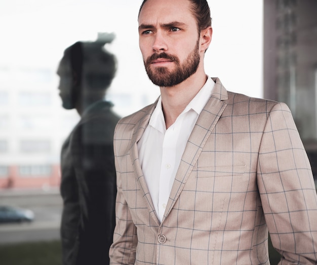 Free photo portrait of sexy handsome fashion male model man dressed in elegant beige checkered suit posing on the street background