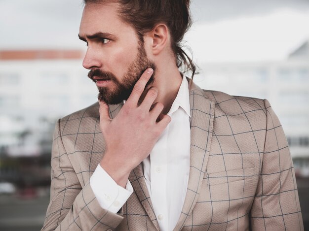 portrait of sexy handsome fashion male model man dressed in elegant beige checkered suit posing on the street background