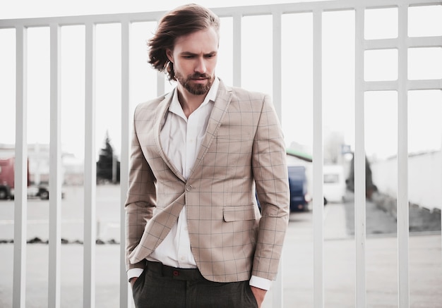 portrait of sexy handsome fashion male model man dressed in elegant beige checkered suit posing on the street background