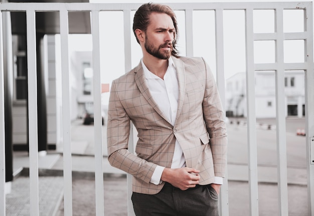 portrait of sexy handsome fashion male model man dressed in elegant beige checkered suit posing on the street background