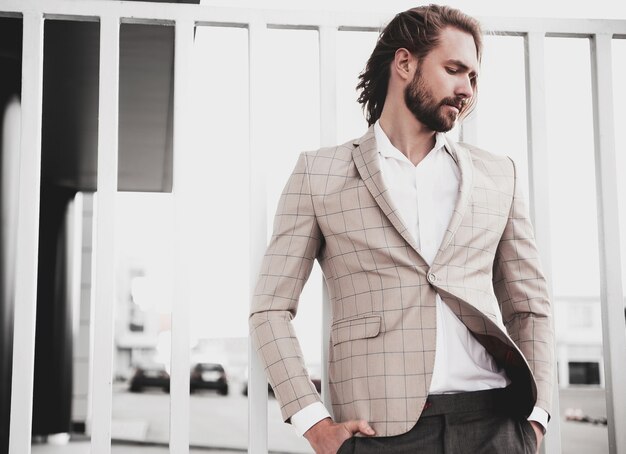 portrait of sexy handsome fashion male model man dressed in elegant beige checkered suit posing on the street background