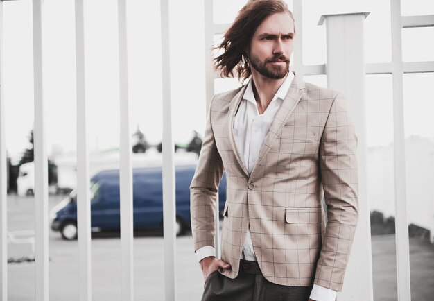 portrait of sexy handsome fashion male model man dressed in elegant beige checkered suit posing on the street background