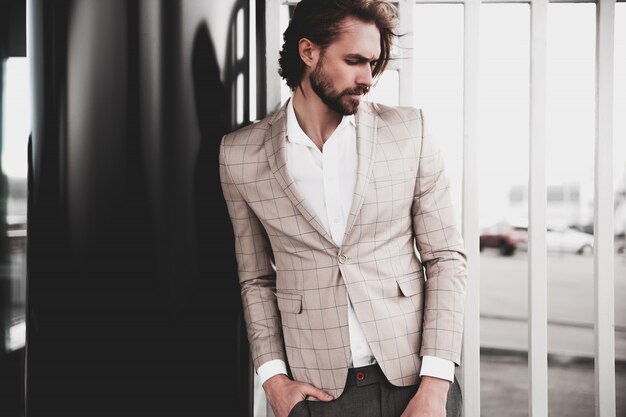 portrait of sexy handsome fashion male model man dressed in elegant beige checkered suit posing on the street background