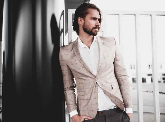 portrait of sexy handsome fashion male model man dressed in elegant beige checkered suit posing on the street background