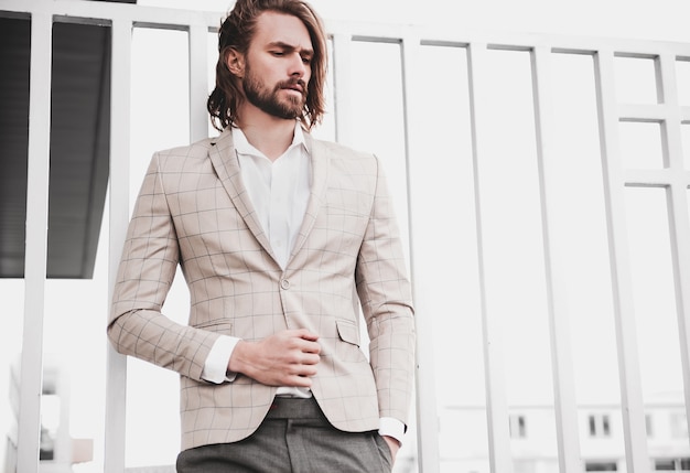 portrait of sexy handsome fashion male model man dressed in elegant beige checkered suit posing on the street background