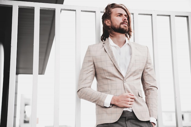 portrait of sexy handsome fashion male model man dressed in elegant beige checkered suit posing on the street background