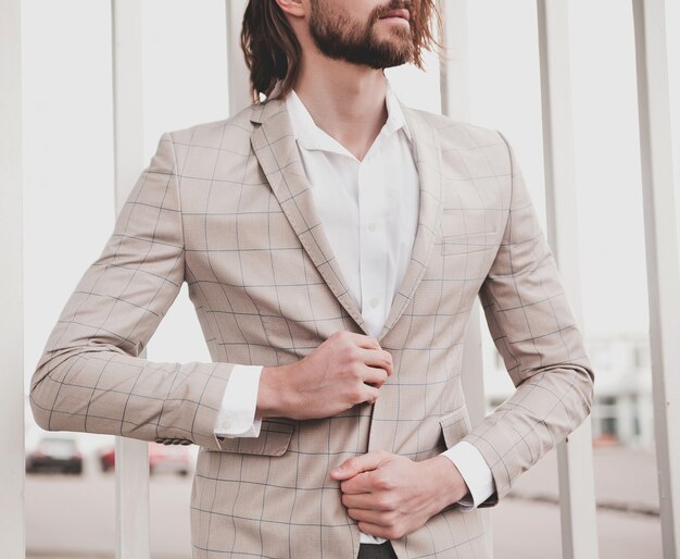 Free photo portrait of sexy handsome fashion male model man dressed in elegant beige checkered suit posing on the street background