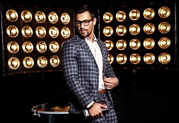 portrait of sexy handsome fashion male model man dressed in elegant suit on black studio lights background in glasses