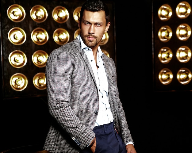 portrait of sexy handsome fashion male model man dressed in elegant suit on black studio lights background