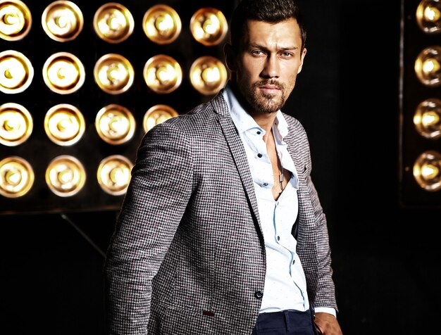 portrait of sexy handsome fashion male model man dressed in elegant suit on studio lights background
