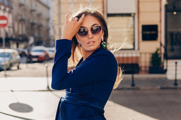 화창한 여름 날에 선글라스를 착용하는 파란색 정장을 입고 거리를 걷는 섹시한 세련된 여자의 초상화