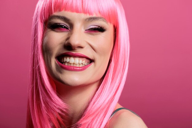 Портрет сексуальной женщины, демонстрирующей искреннюю идеальную улыбку на камеру, чувствующую себя счастливой и позитивной. Модель улыбается и имеет белые зубы, красивый макияж и парик с розовыми волосами, чтобы чувствовать себя красивой.
