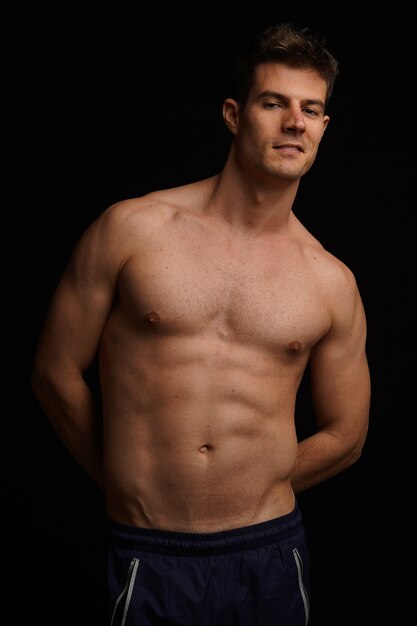 Portrait of a shirtless athletic young Hispanic male posing against a black wall