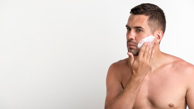 Portrait of shirtless man applying foam while shaving