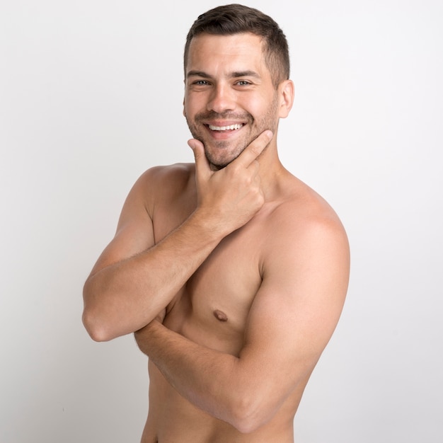 Portrait of shirtless smiling young man keeping hand on chin and looking at camera