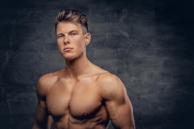 Portrait of shirtless strong suntanned muscular male over grey background.