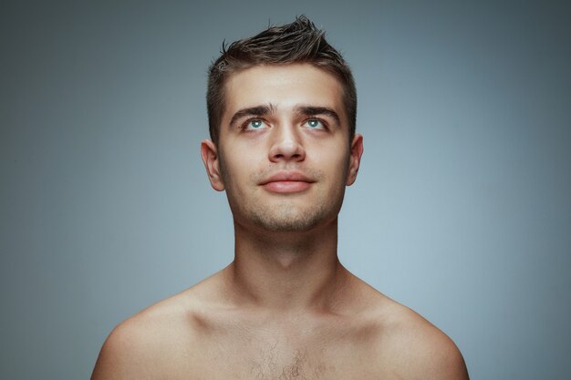 Portrait of shirtless young man isolated on grey studio background. Caucasian healthy male model looking up and posing. Concept of men's health and beauty, self-care, body and skin care.