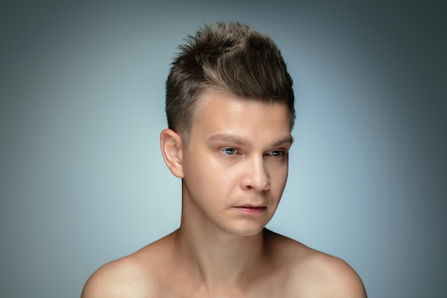 Portrait of shirtless young man isolated on grey  wall. Caucasian healthy male model looking at side and posing. Concept of men's health and beauty, self-care, body and skin care.