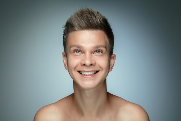 Portrait of shirtless young man isolated on grey  wall. Caucasian healthy male model looking up and posing. Concept of men's health and beauty, self-care, body and skin care.