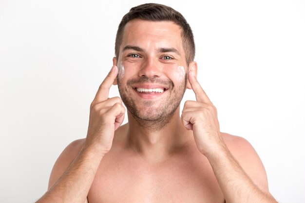 Portrait of shirtless young man massaging with cream against white background