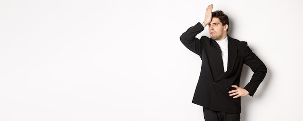 Free photo portrait of shocked and distressed businessman in black suit slap forehead and looking anxious stand
