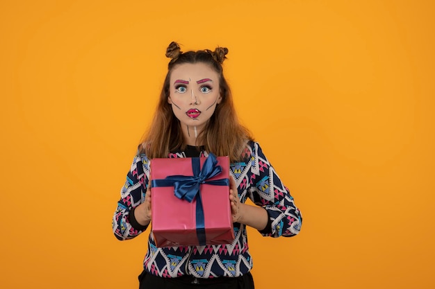 Портрет шокированной девушки с креативным макияжем и подарочной коробкой. Фото высокого качества
