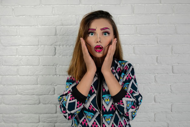 Portrait of shocked girl wearing creative makeup and holding hands to her face. high quality photo