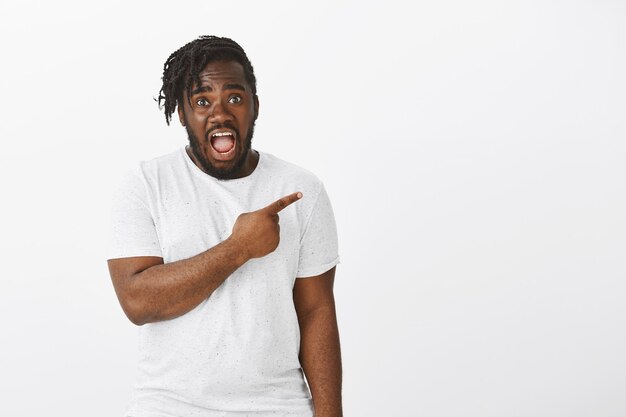 Portrait of shocked guy with braids posing against the white wall