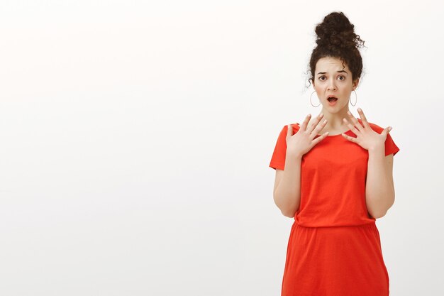 Portrait of shocked stunned attractive european woman in casual red dress, gasping with opened mouth