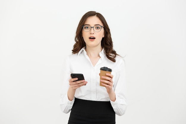 Portrait of a shocked surprised businesswoman in eyeglasses holding take away coffee cup and mobile