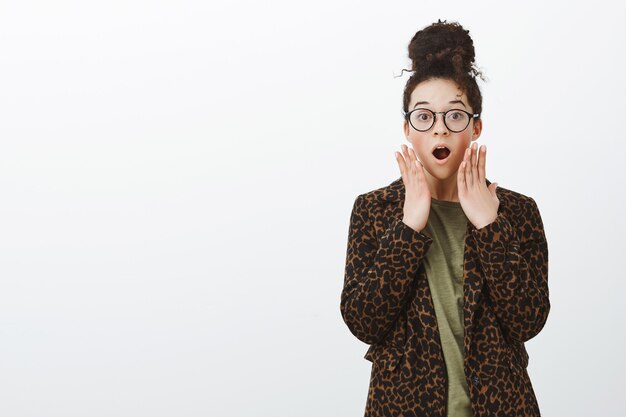 Portrait of shocked surprised girlfriend in leopard coat and black trendy glasses, dropping jaw, saying wow and holding palms near mouth