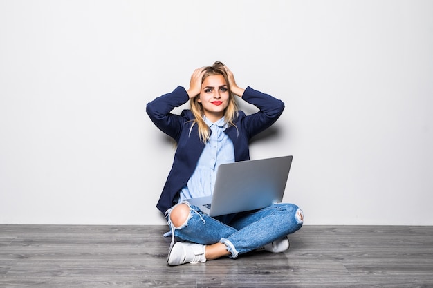 Portrait of shocked woman sitting on the floor with laptop and looking on gray wall