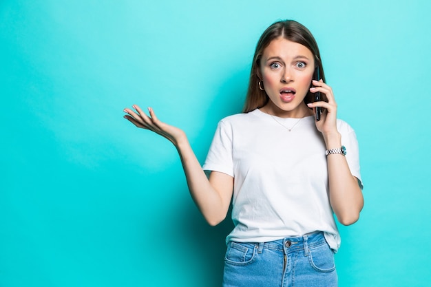 Portrait of a shocked young girl talk mobile phone isolated