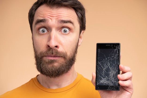 Ritratto di un giovane scioccato che mostra il suo smartphone rotto
