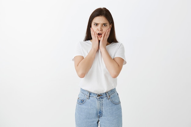 Portrait of shocked young woman posing against white wall