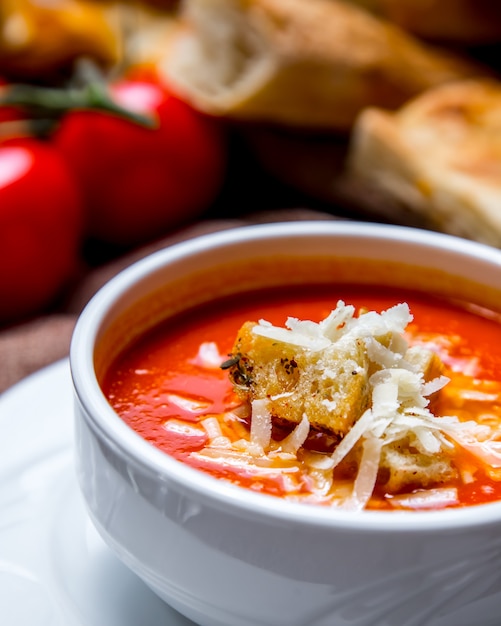 Портретная съемка томатного супа с крекерами и сыром, помидорами и хлебом на столе