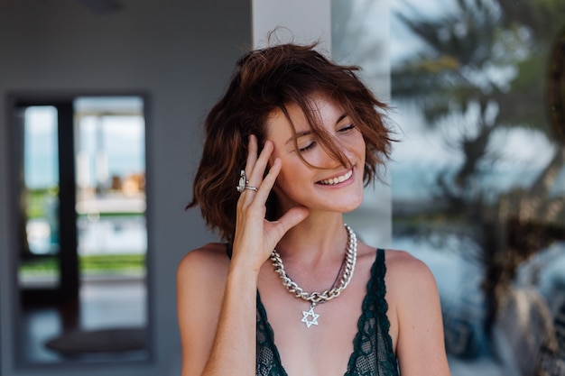 Portrait of short hair brunette woman with chain on neck accessories in green lace lingerie outside villa