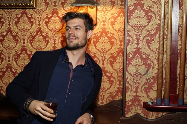 Free photo portrait shot of an intelligent businessman holding whiskey in his hand and smiling confidently